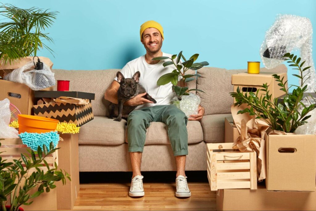 A man and his pup sit on the sofa in their new home. There are dangerous houseplants that can harm your pup if you do not take preventative measures.